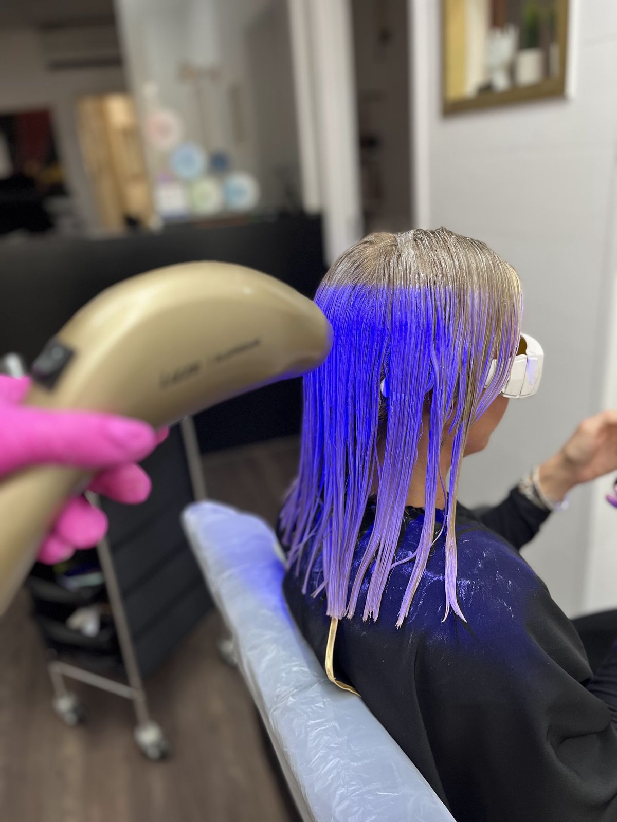 Een haarbehandeling in uitvoering: nat haar onder paars licht en een gouden behandelapparaat